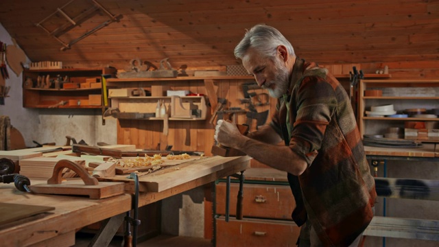 一位年长的男木匠正在他的店里用刨子刨出一块方正的木板视频下载