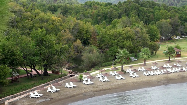土耳其地中海海滩绿树旁的躺椅。视频下载