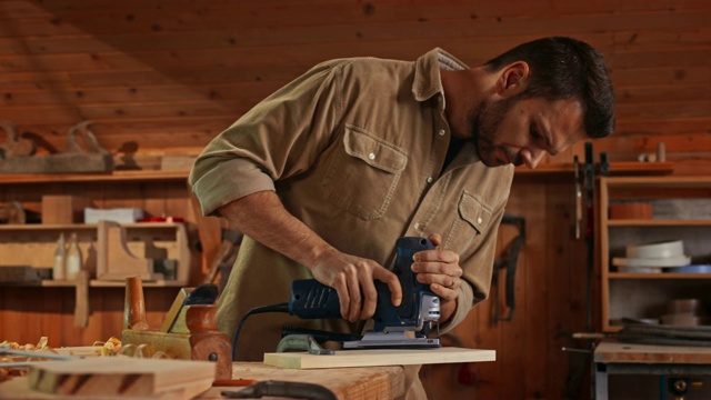 年轻的男木匠在他的店里用拼图锯切一块木头视频素材