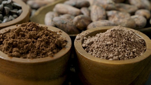 三个木碗里放着热巧克力粉，可可粉和巧克力块，旁边放着可可豆。旋转。视频素材