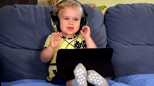 可爱的学步女孩戴着耳机用平板电脑听音乐视频素材