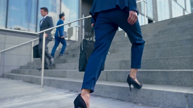 SLO MO TS一个女人的腿，穿着商务套装和高跟鞋走上现代办公大楼外的楼梯视频素材