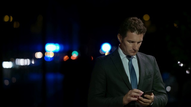 一个白人商人晚上站在外面用智能手机打字视频素材