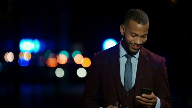 LD年轻的混血企业家晚上站在外面用智能手机打字，面带微笑视频素材