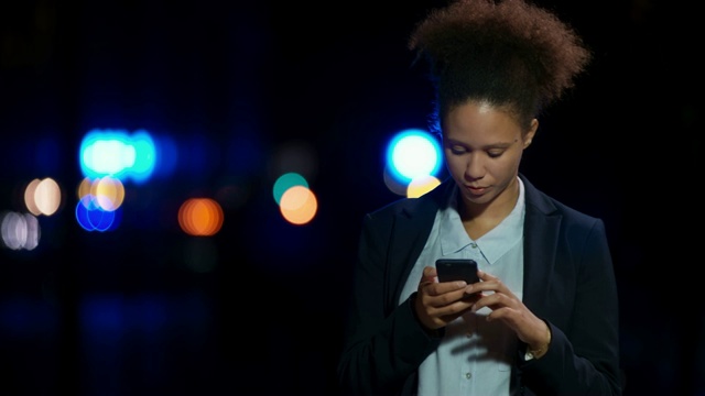 LD年轻的混血女企业家晚上站在外面用智能手机打字，面带微笑视频素材
