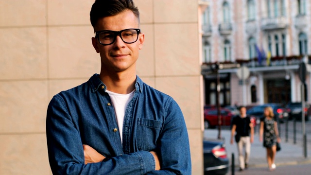 肖像中的年轻时尚男子在休闲衬衫交叉手，看着相机在城市和微笑。视频下载