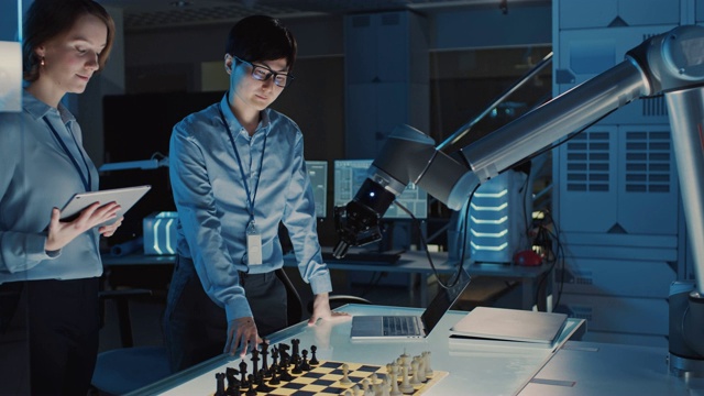 两名开发工程师正在讨论和测试一个人工智能界面，方法是用一个未来机器人手臂下棋。他们在一个高科技现代研究实验室。视频素材