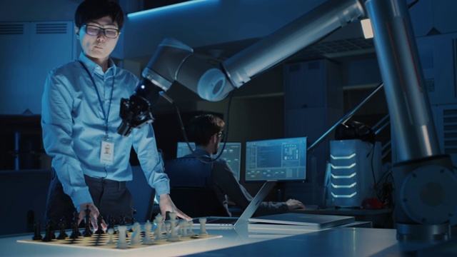 专业的日本开发工程师正在测试一个人工智能界面，用一个未来的机械臂下棋。他们在一个高科技现代研究实验室。视频素材