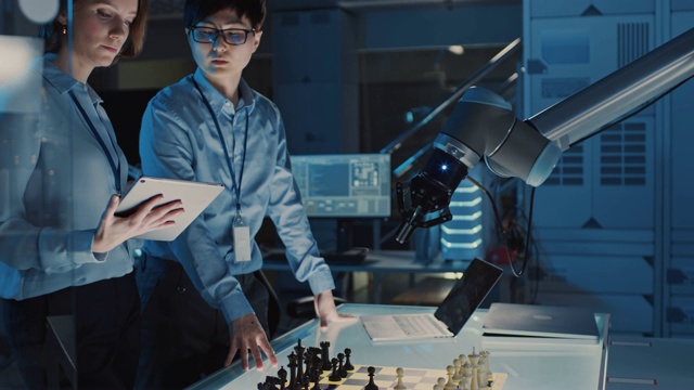 两名开发工程师正在讨论和测试一个人工智能界面，方法是用一个未来机器人手臂下棋。他们在一个高科技现代研究实验室。视频素材