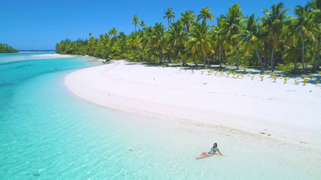 航拍:一名身穿比基尼的年轻女子在太平洋郁郁葱葱的热带岛屿上晒日光浴。视频下载