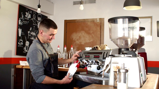 一个在咖啡店里蒸着白咖啡杯的男咖啡师的特写。视频下载