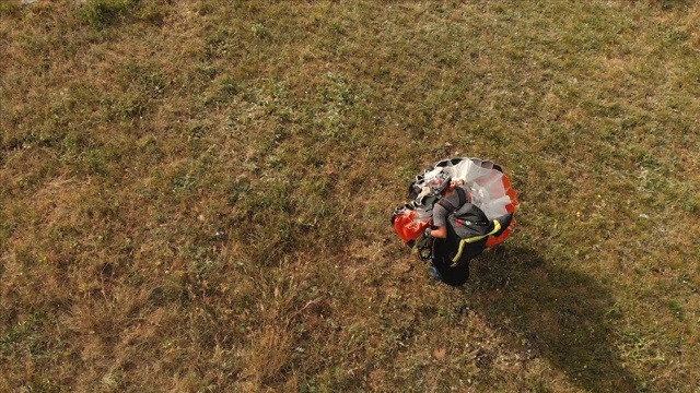 专业滑翔伞降落后的鸟瞰图，将滑翔伞放在肩膀上，从山坡上走下来，到达发射地点。Paraglide运动视频下载