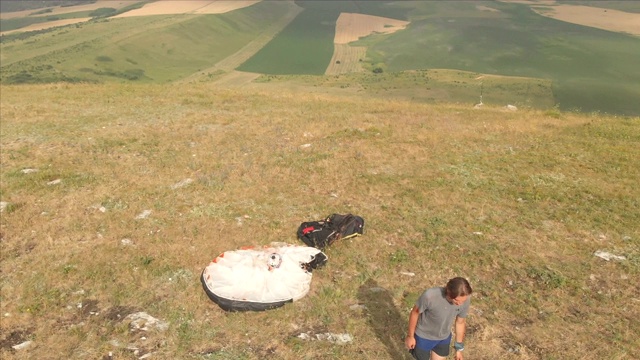 鸟瞰图专业滑翔伞降落后，起飞设备和头盔，去一个山坡。滑翔伞运动视频下载