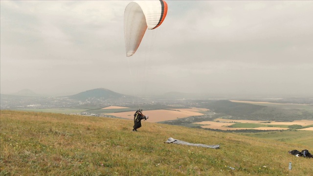 鸟瞰图专业滑翔伞降落后，起飞设备和头盔，去一个山坡。滑翔伞运动视频下载