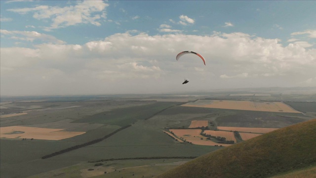 一个滑翔伞运动员坐在燕子旁边的滑翔伞上飞行。无人机后续拍摄视频素材