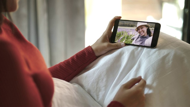年轻女子拿着智能手机摄像头与躺在家里床上的朋友视频聊天视频素材