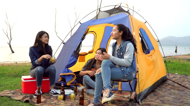 手持式正面视图:三个女人花周末时间露营和一起在日落的水边喝酒视频素材