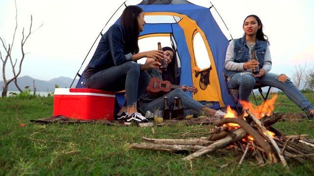 低角度正面视图:三个女人花周末时间露营和一起在日落的水边喝酒视频素材