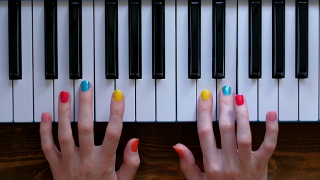 一个年轻积极的女孩与美丽的手和颜色美甲弹钢琴视频素材