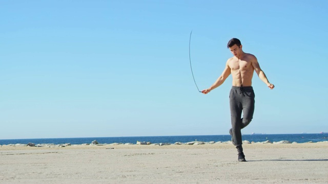 赤裸上身的肌肉运动员在海滩上跳绳视频下载