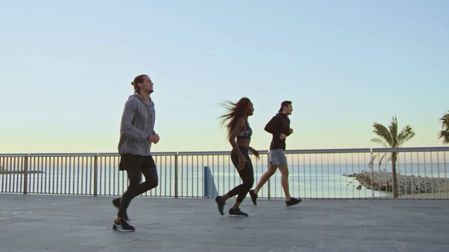 日落时，运动员在海边的散步道上慢跑视频下载