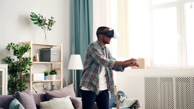 一名非裔美国男子戴着虚拟现实眼镜在家玩游戏视频素材
