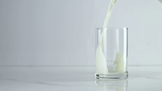 慢镜头:将牛奶倒入白色背景的玻璃杯中。视频下载
