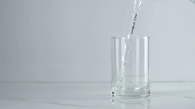 慢动作:在白色背景下将水倒进玻璃杯。视频素材