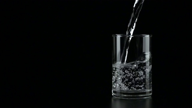 慢动作:在黑色背景下将水倒进玻璃杯。视频素材