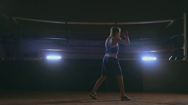 一位美丽的女子在进行影子格斗时，一边练习击球的技术和速度，一边为将来的胜利而努力训练。黑暗的健身房背景。替身拍摄视频素材