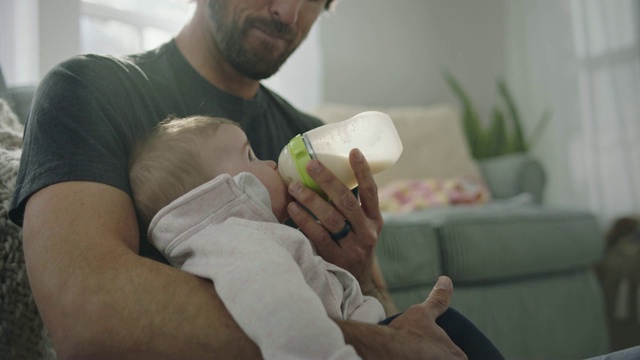 一位居家爸爸微笑着用奶瓶喂他的宝宝。视频下载
