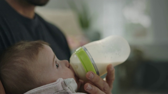 镜头从父亲微笑的脸上倾斜下来，婴儿的女儿正在喂奶。视频素材