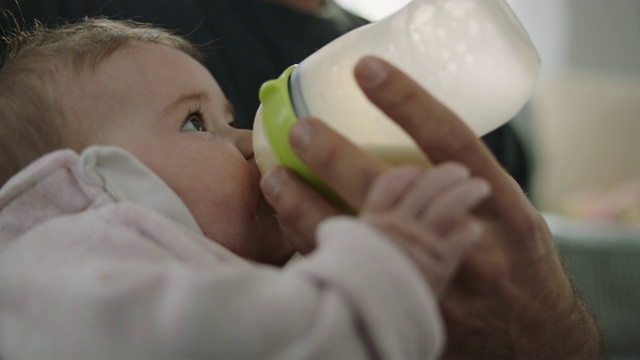 小宝贝睁大了眼睛，握着爸爸的手，喝着奶瓶里的牛奶。视频素材