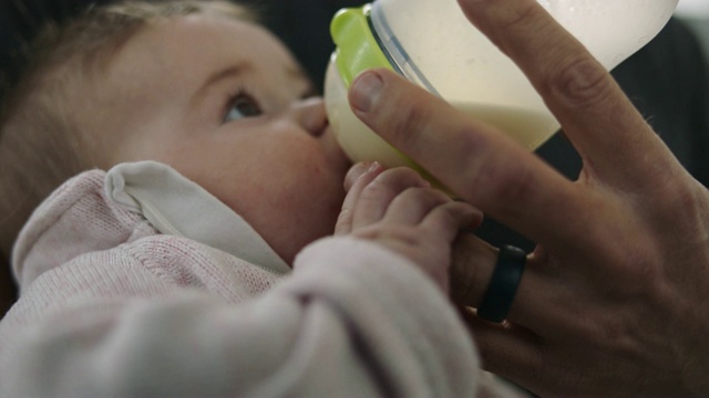 小女孩用小手搂住爸爸的手指，喝着奶瓶里的牛奶。视频素材