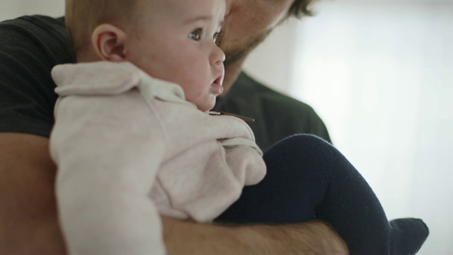 可爱的女婴看着镜头，父亲把她抱在怀里，亲吻她的额头。视频素材