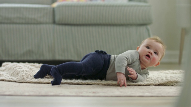 可爱的小女孩伸出舌头，在客厅地板上柔软的毯子上前后翻滚。视频素材