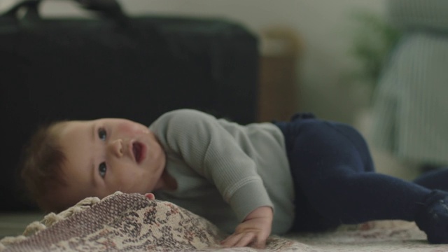 铜。可爱的宝宝双手抱着脚，在客厅的地毯上翻滚。视频素材