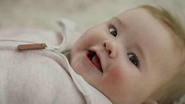 可爱的女婴躺在她的背上，惊奇地抬头看着镜头，微笑着。视频素材