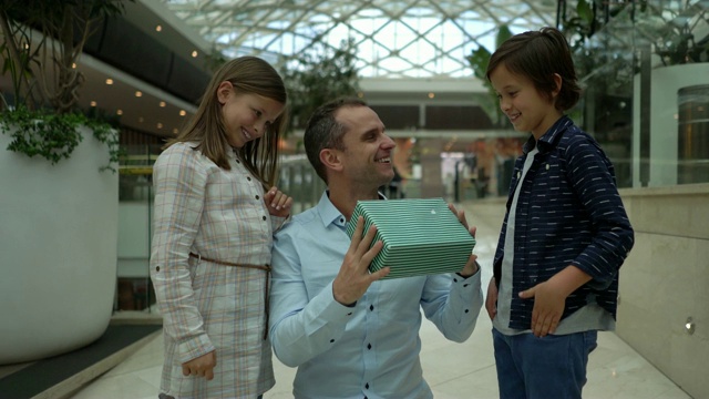 儿子和女儿在购物中心给他们的父亲一个惊喜，在父亲节的礼物，他拥抱他们和微笑视频下载