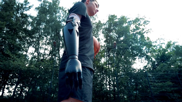 一个带着机器人假肢的残疾人站在篮球场上，拿着一个球。视频下载
