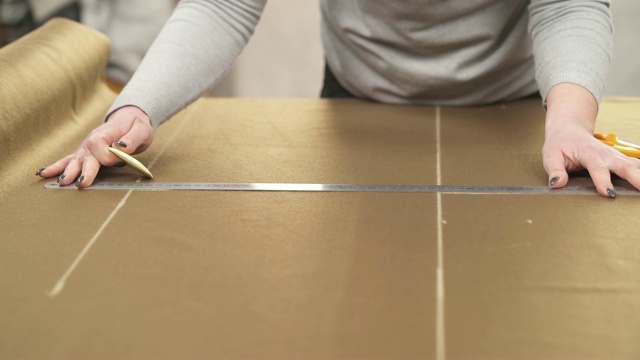 一个裁缝用尺子在深棕色的织物上用粉笔做图案的特写。视频素材