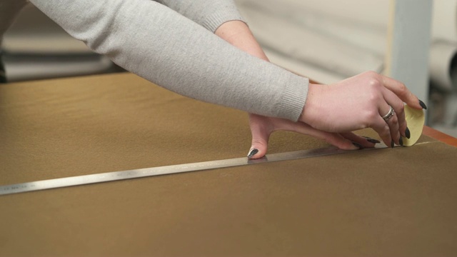 裁缝用尺子在材料上用粉笔做一个图案。在画室里，裁缝从一大束棕色的织物上制作一件物品。视频素材