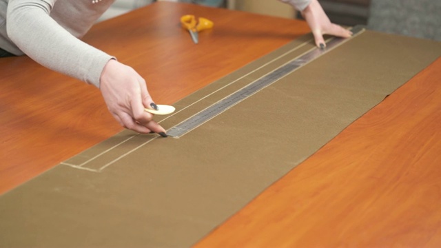 一名专业设计师在工作室工作，用粉笔在棕色材料上用尺子做一个图案的侧视图。视频素材