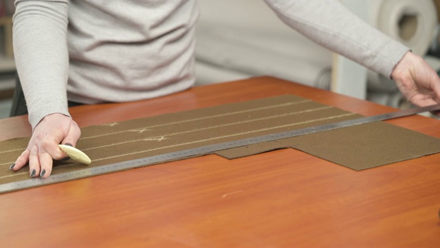 一位专业裁缝用尺子在棕色材料上用粉笔做图案的侧面图。她正在量材料并做标记，准备切割。视频素材