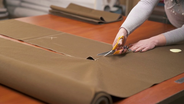 一名裁缝根据图样用专业剪刀剪一大块棕色织物视频素材