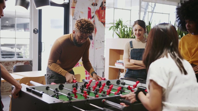 千禧一代的商业创意人士在工作中玩桌上足球来休息视频素材