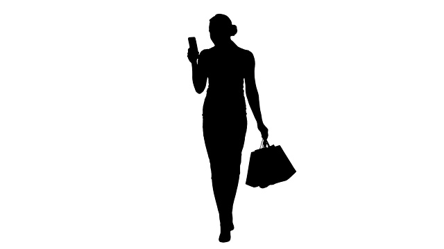 轮廓美丽迷人的女人看智能手机和拿着购物袋走时视频素材