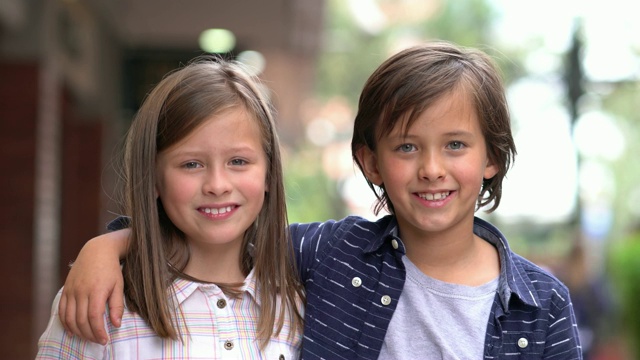 可爱的小弟弟和小妹妹在商场里对着镜头微笑，头靠在一起视频下载