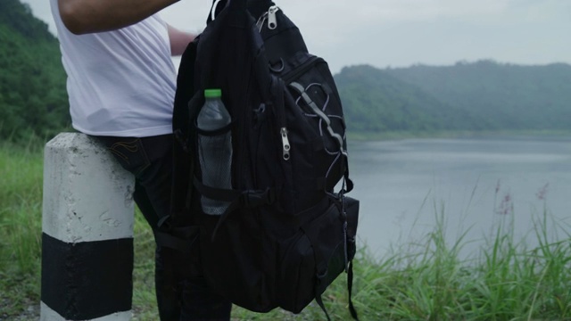 徒步旅行者背包男子徒步冒险感觉自由行走在森林附近的湖在雨天。生活方式男人旅游放松的概念。视频购买