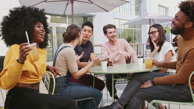 六个时髦的千禧一代朋友坐在咖啡馆外的街上喝着冷啤酒聊天视频素材